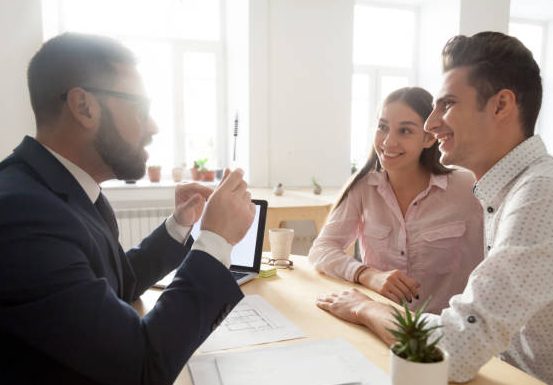 Male architect or interior designer gesturing discussing house project with excited millennial couple, realtor talking with young spouses about mortgage loan or purchase, consulting about offers